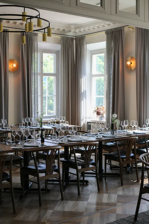The banquet hall laid for dinner, with tall windows and chandeliers