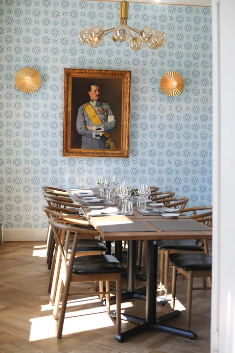 The private dining room with blue patterned wallpaper, a portrait and laid tables