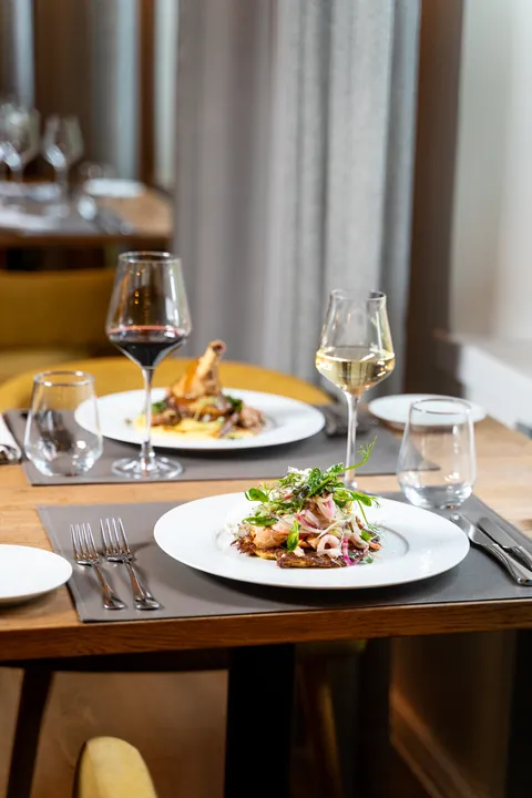 Two plates and wine glasses on a laid table beside the window curtain