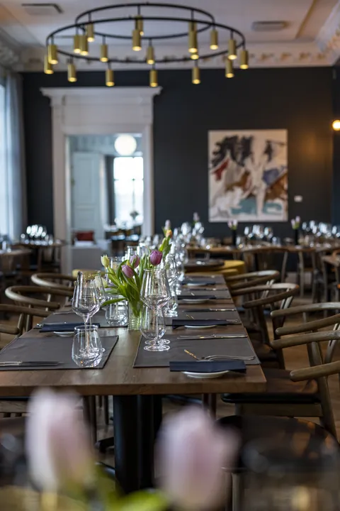 A long laid table in front of tall windows, tulips in the foreground