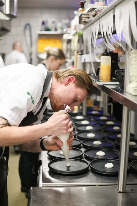 A chef finishing plates along the pass